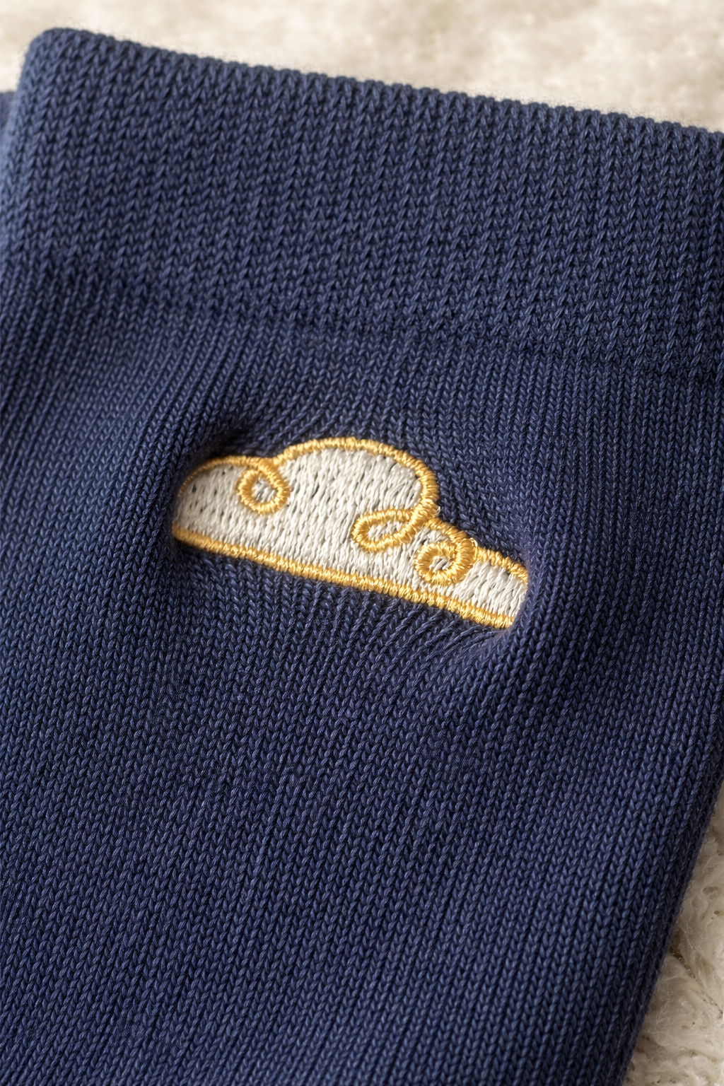 Close-up of navy baby sock with gold cloud embroidery on soft knitted fabric