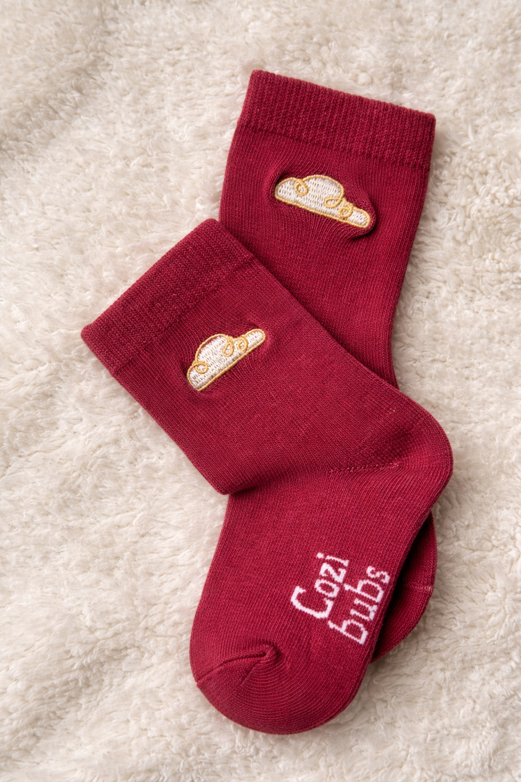 Pair of baby cotton socks in berry with Cozibubs logo and gold cloud embroidery on neutral background