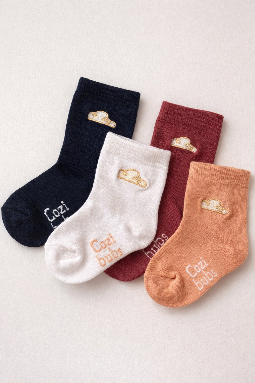 Set of baby cotton socks in cream, navy, berry and peach with Cozibubs logo and cloud embroidery on neutral background