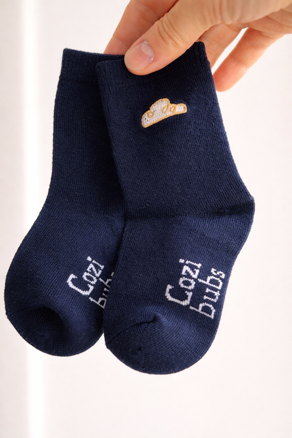 Baby cotton socks in navy with Cozibubs logo and cloud embroidery, held by hand on neutral background