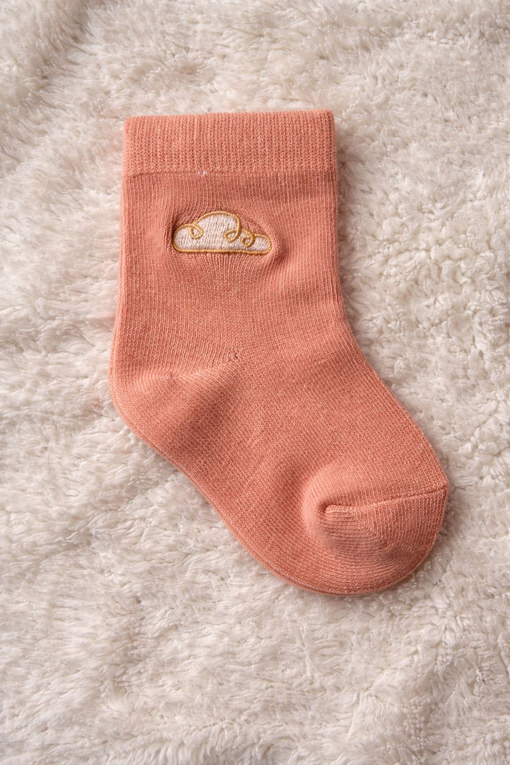 Baby cotton sock in peach with gold cloud embroidery on soft textured background