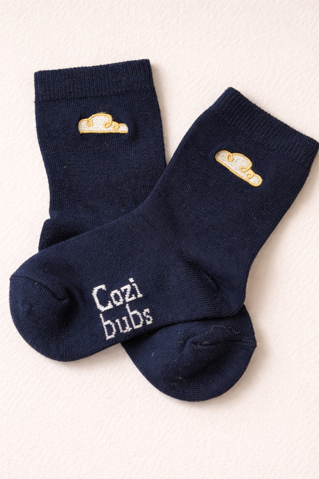 Baby cotton socks in navy with Cozibubs logo and gold cloud embroidery on neutral background