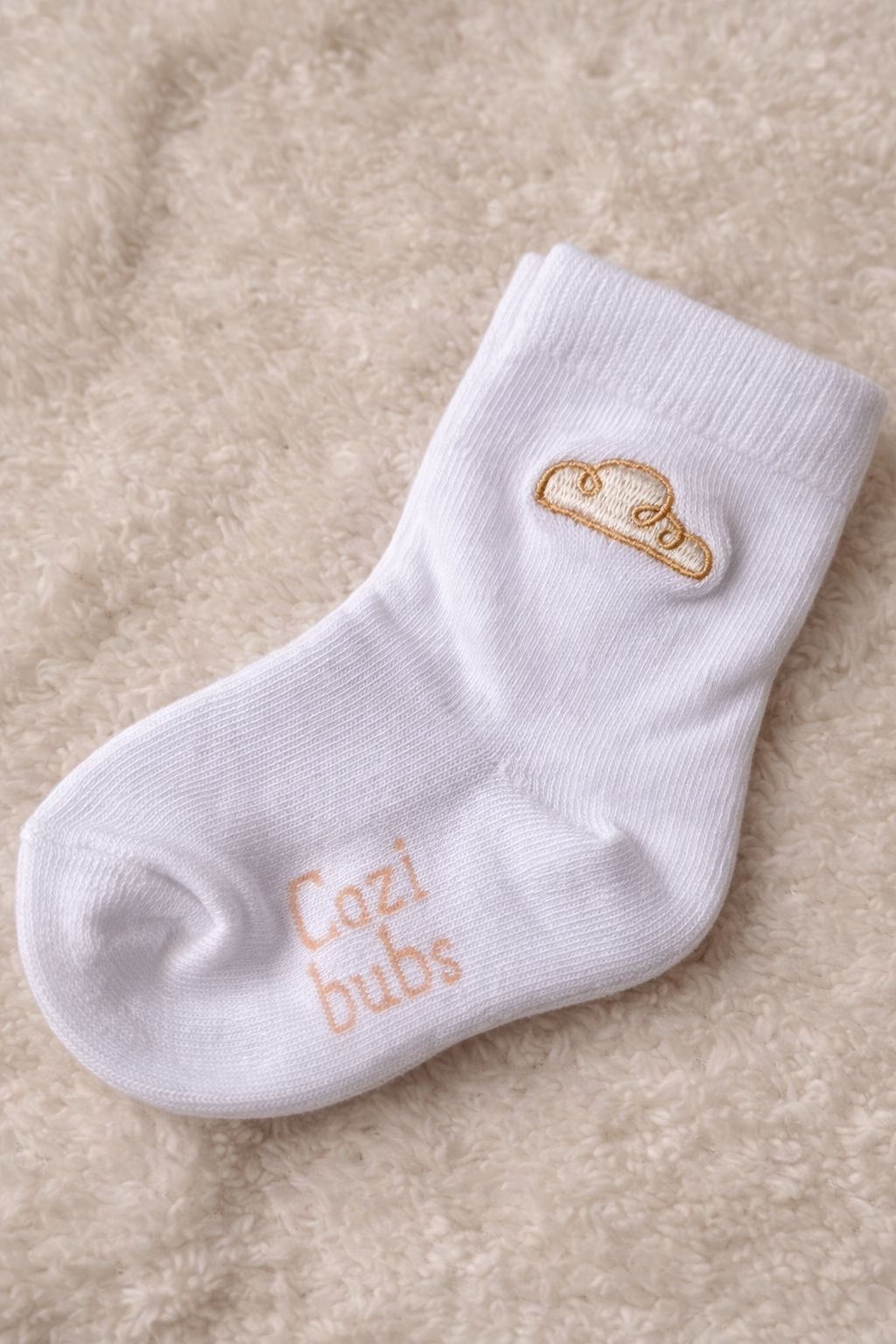 Baby cotton sock in cream with Cozibubs embroidery on soft neutral background