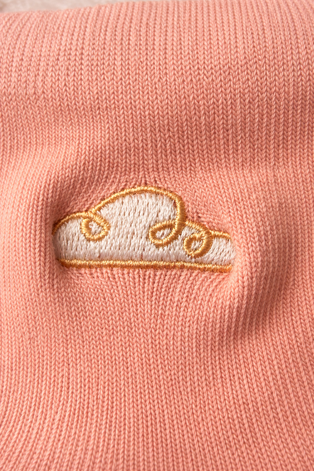 Close-up of peach baby sock with gold cloud embroidery on soft knitted fabric