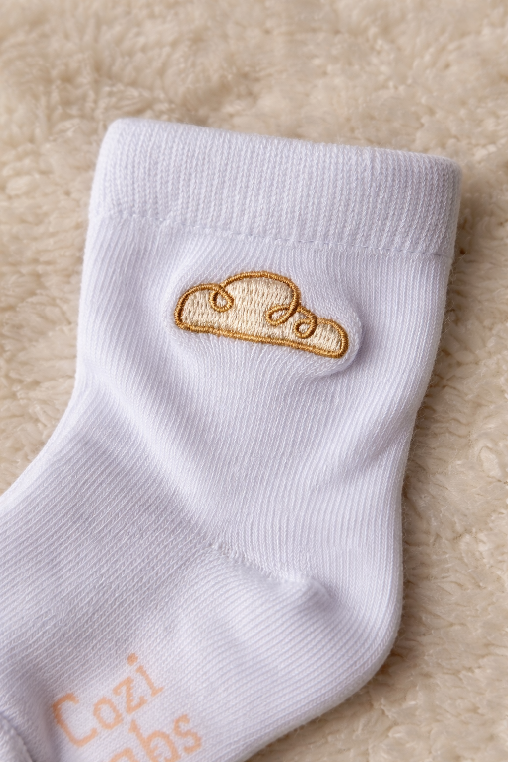 Baby cotton sock in cream with gold cloud embroidery detail on soft textured background