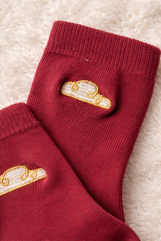 Close-up of berry baby sock with gold cloud embroidery on soft knitted fabric