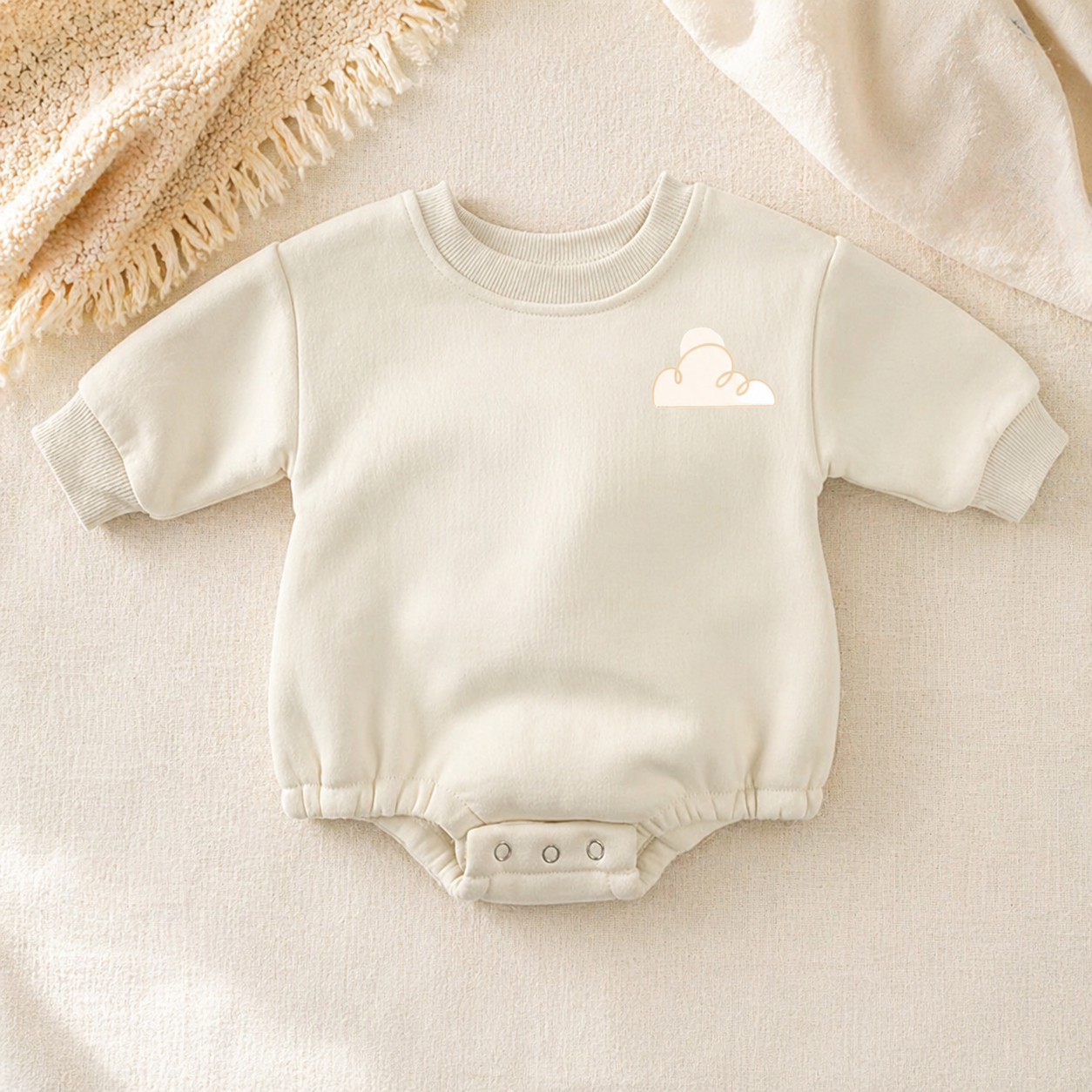 Cream fleece baby romper with minimal cloud embroidery, styled on a soft beige textured blanket in warm neutral lighting.