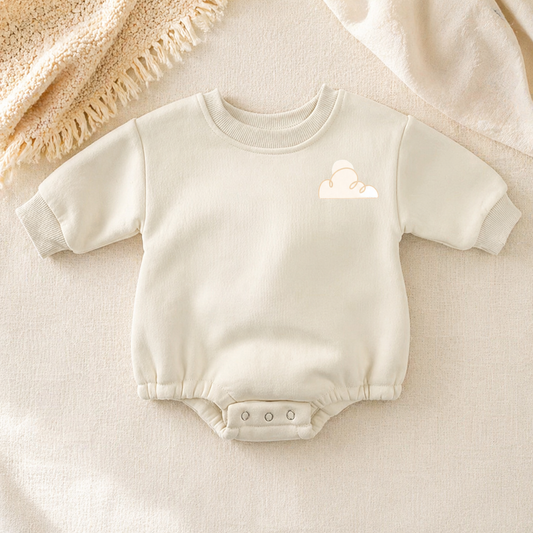 Cream fleece baby romper with minimal cloud embroidery, styled on a soft beige textured blanket in warm neutral lighting.