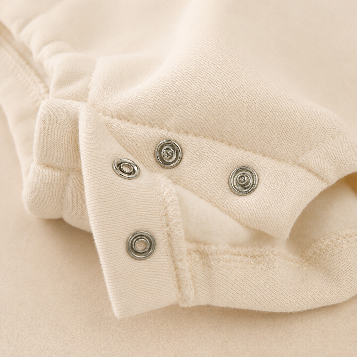 Soft cream fleece baby romper with snap button closure and plush cotton lining, photographed in warm neutral lighting against a soft beige background.