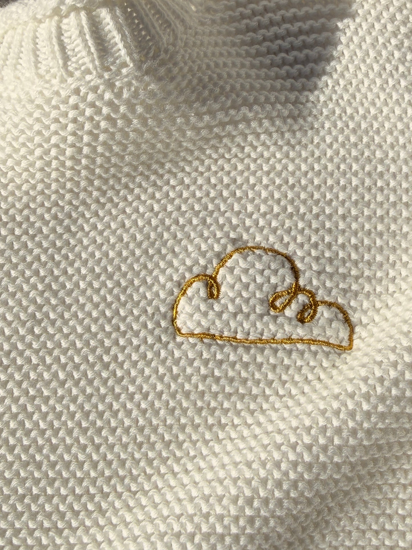 Close-up of the embroidered gold cloud logo on the Bubs on Cloud cream sweater.